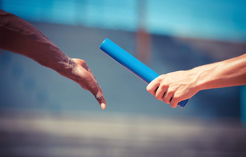 Close-up of two hands passing a relay baton.