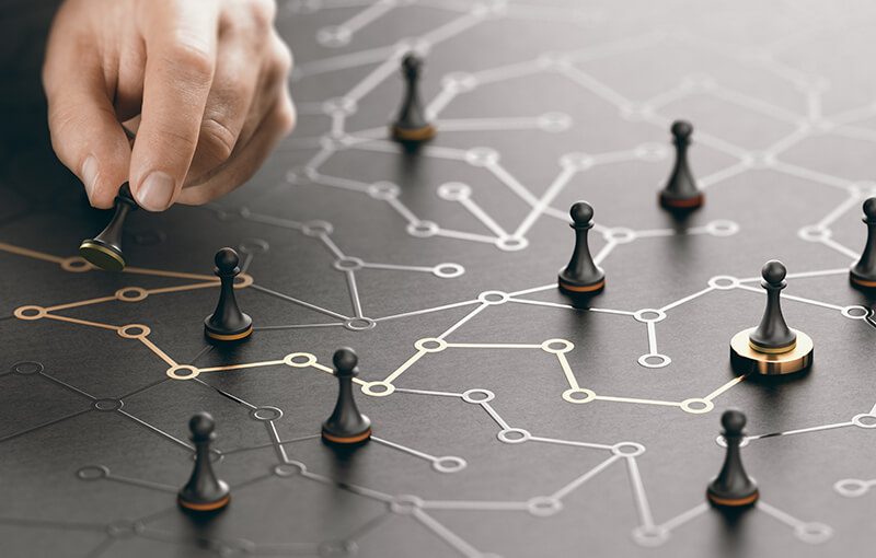 Multiple chess pawns scattered on a dark wooden surface which has lines connected by circles drawn on it. One of the connected lines is colored in gold.