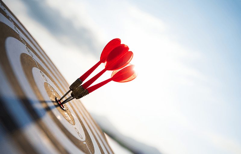 Three red darts in the center of a target, against a blue sky.