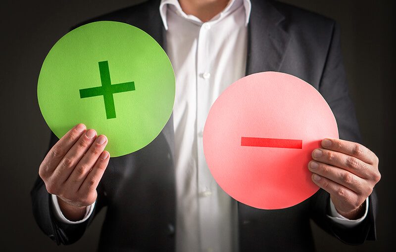A person holding up two circles; one is green with a "plus" sign and one is red with a "minus" sign