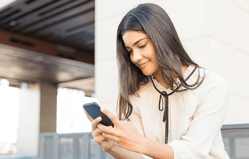 Young woman sits on steps, holding and looking at her mobile phone