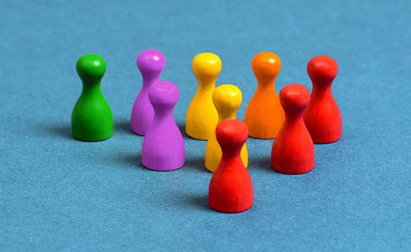 Nine multicolored wooden game pawns sitting on a blue-grey surface.