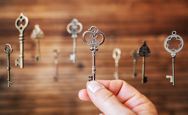 Multiple keys floating in front of a wood background. A hand is seen reaching out and choosing one of the keys.
