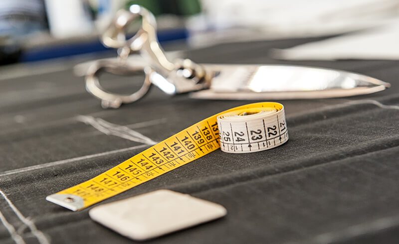 A pair of scissors and a tape measure sitting on a piece of dark grey fabric.