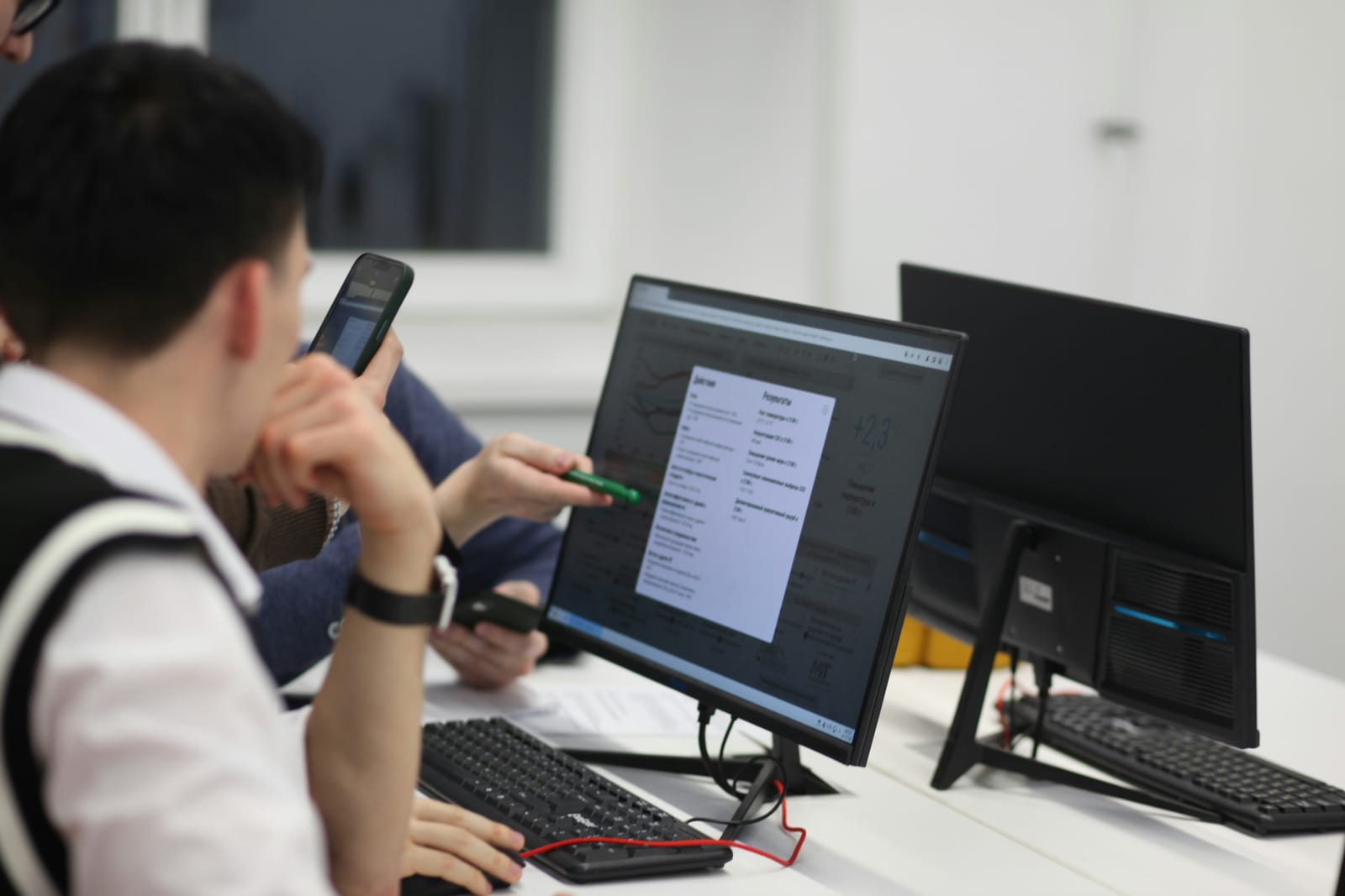 A man with a phone in hand, focused on the work across his two monitors