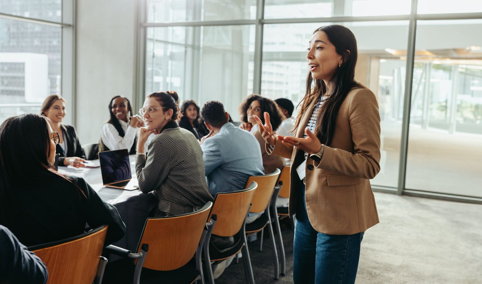 A woman presenting to a seated team in a bright glass meeting room