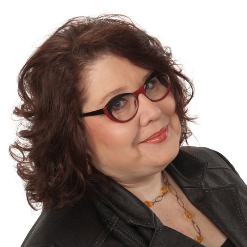 Susan Hurrell, smiling, with curly auburn hair and red glasses, in a dark jacket